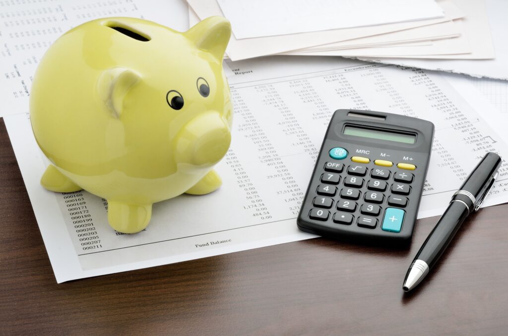 A piggybank, calculator, pen, and some financial sheets on a desk.