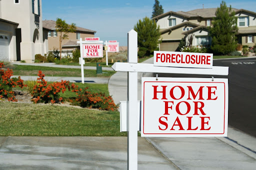 A row of houses with “For Sale - Foreclosure” signs.