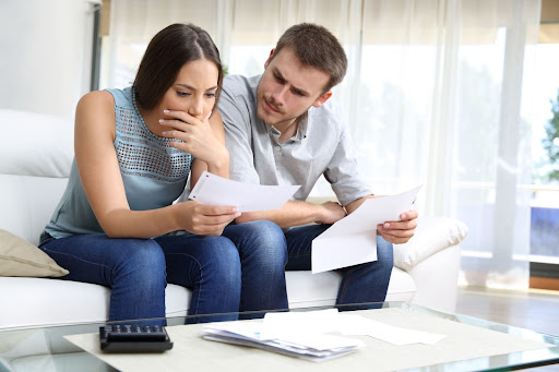 A worried-looking couple sits on the sofa and checks a receipt.